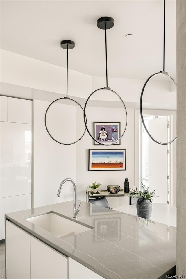 kitchen with hanging light fixtures, dark stone countertops, sink, and white cabinets