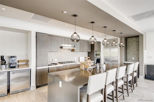 kitchen featuring pendant lighting, tasteful backsplash, a center island with sink, appliances with stainless steel finishes, and a breakfast bar area