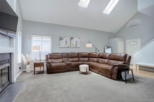 living room with high vaulted ceiling, a skylight, a tiled fireplace, and dark carpet