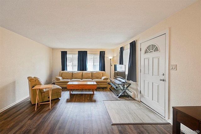 living room featuring a textured wall, dark wood-style floors, and baseboards