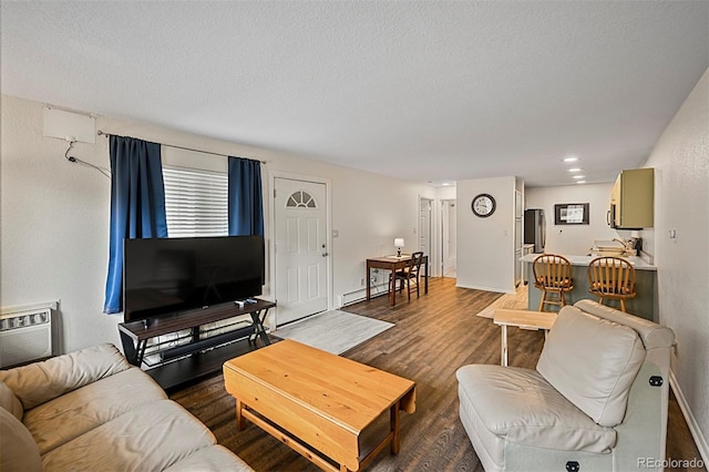 living room with dark wood-type flooring, a textured ceiling, baseboard heating, an AC wall unit, and baseboards