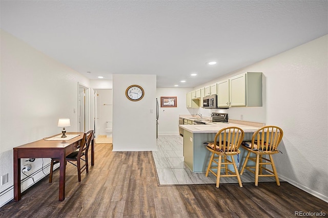 kitchen featuring baseboards, light countertops, appliances with stainless steel finishes, a kitchen bar, and wood finished floors
