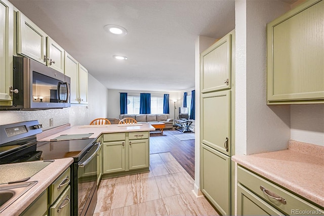 kitchen with stainless steel appliances, open floor plan, a peninsula, light countertops, and green cabinetry