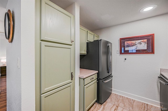 kitchen featuring baseboards, green cabinetry, light countertops, freestanding refrigerator, and recessed lighting