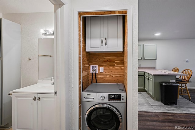 washroom with a textured wall, washer / clothes dryer, a sink, and wood finished floors