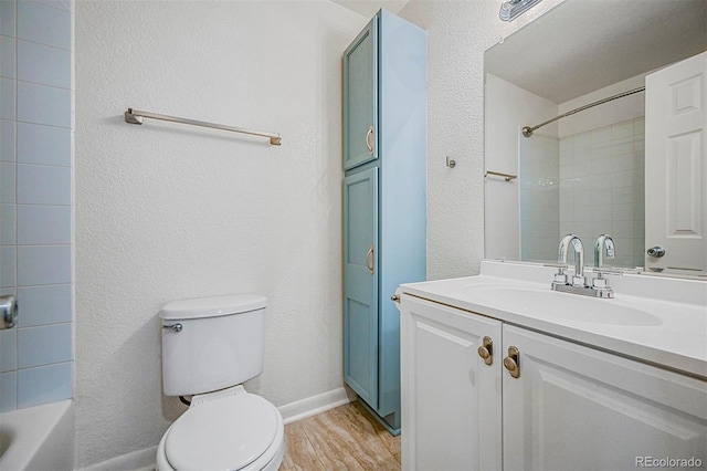 bathroom with vanity, baseboards, a textured wall, toilet, and wood finished floors