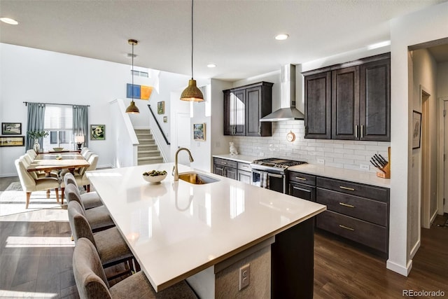 kitchen featuring sink, stainless steel gas range, decorative backsplash, wall chimney range hood, and a kitchen island with sink