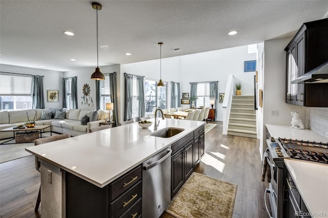 kitchen featuring sink, decorative light fixtures, light wood-type flooring, an island with sink, and appliances with stainless steel finishes