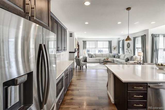 kitchen with stainless steel appliances, dark brown cabinets, a kitchen island, and hanging light fixtures