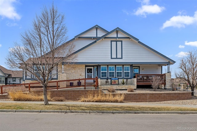 view of front of property featuring stone siding, a porch, and fence