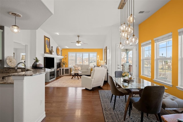 dining space featuring visible vents, a fireplace, lofted ceiling, ceiling fan, and dark wood-style flooring