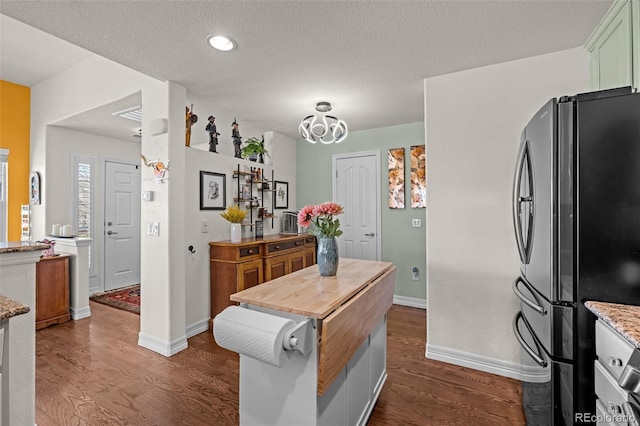 kitchen with dark wood-type flooring, baseboards, freestanding refrigerator, and a textured ceiling