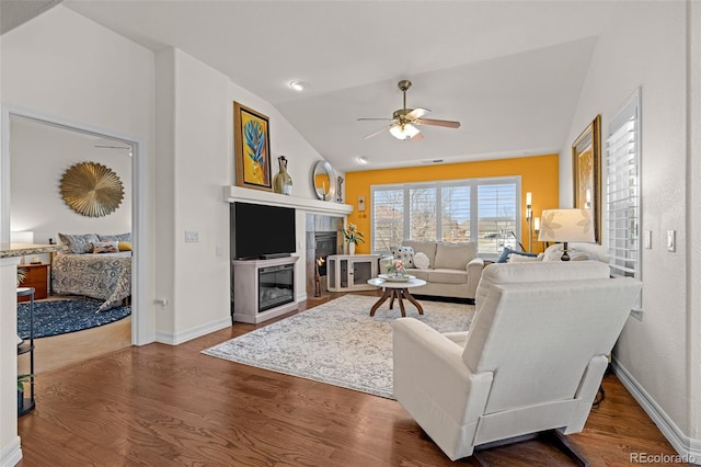 living area with a ceiling fan, wood finished floors, baseboards, lofted ceiling, and a fireplace