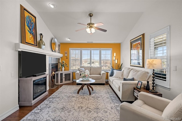 living room with a ceiling fan, baseboards, dark wood finished floors, lofted ceiling, and a glass covered fireplace