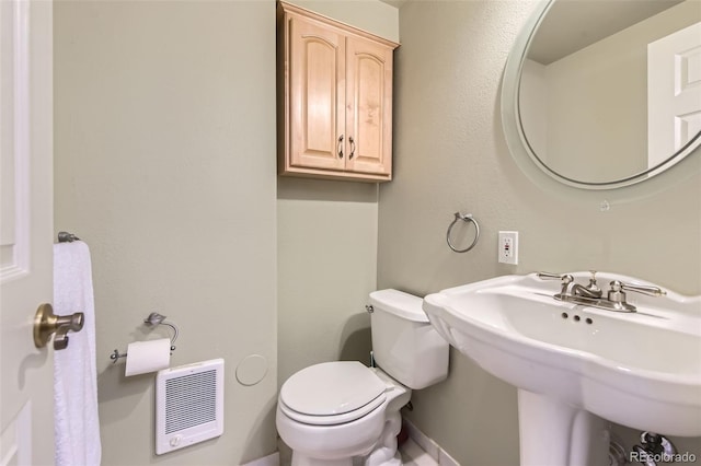 bathroom with toilet, heating unit, and sink