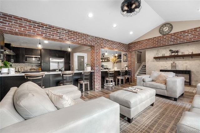living area with vaulted ceiling, stairway, wood finished floors, brick wall, and recessed lighting