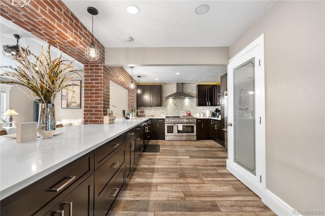 kitchen with double oven range, light wood finished floors, wall chimney exhaust hood, light countertops, and dark brown cabinets