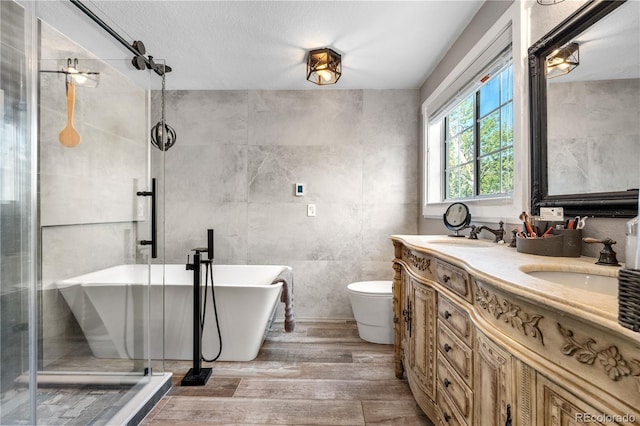 bathroom with wood finished floors, a freestanding bath, double vanity, tile walls, and toilet
