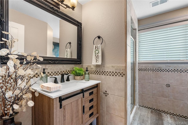 bathroom with tile walls, a shower stall, vanity, wainscoting, and wood finished floors