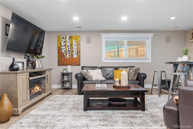 living room with light wood finished floors, a warm lit fireplace, recessed lighting, and baseboards