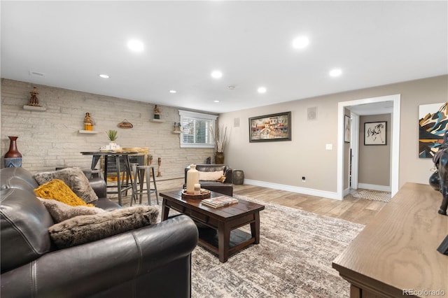 living area featuring baseboards, light wood finished floors, recessed lighting, and brick wall