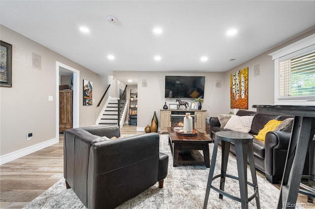 living area featuring stairs, light wood-style floors, recessed lighting, a warm lit fireplace, and baseboards