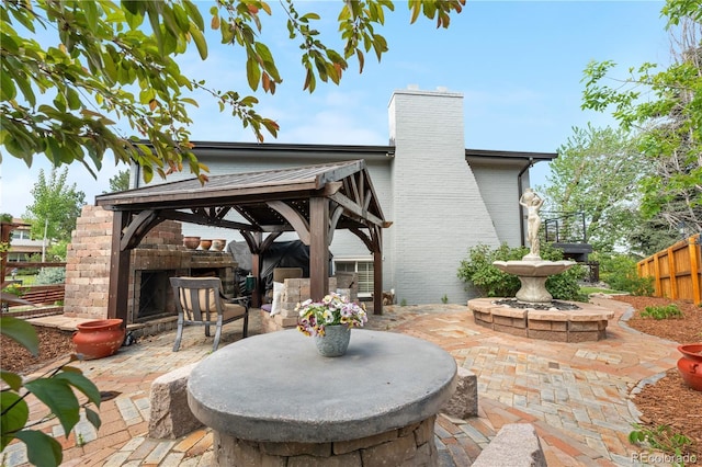 view of patio featuring an outdoor brick fireplace, fence, and a gazebo