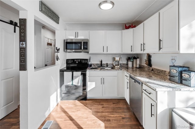 kitchen featuring stone counters, appliances with stainless steel finishes, dark hardwood / wood-style floors, white cabinets, and a barn door