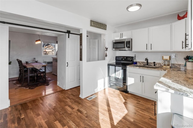 kitchen with black / electric stove, dark hardwood / wood-style floors, a barn door, and white cabinets