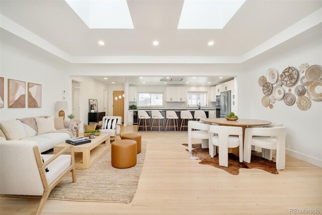 living room with recessed lighting, a skylight, baseboards, and light wood-style floors