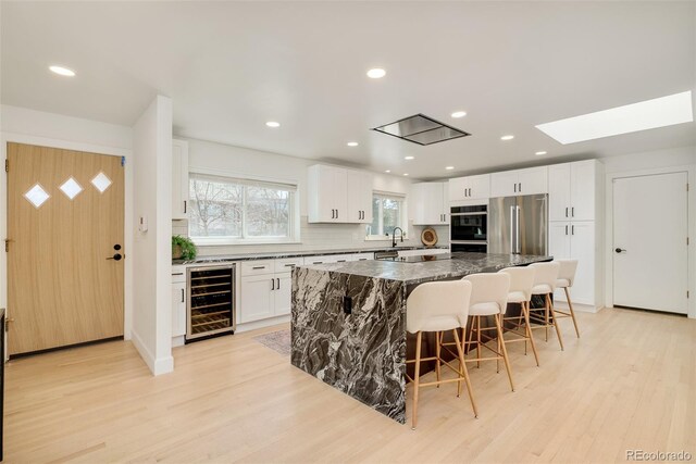 kitchen featuring a breakfast bar area, a kitchen island, high quality fridge, beverage cooler, and light wood-style flooring