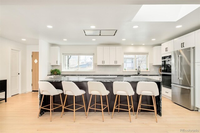 kitchen featuring a sink, a breakfast bar area, light wood-style flooring, tasteful backsplash, and high quality fridge