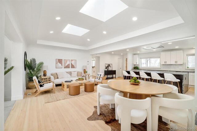 dining area featuring light wood-type flooring, recessed lighting, and a raised ceiling