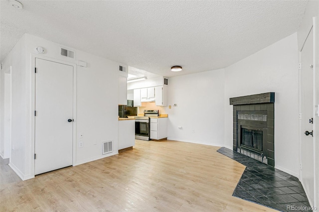 living area featuring a tiled fireplace, visible vents, and light wood finished floors