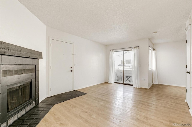 unfurnished living room with a tiled fireplace, wood finished floors, baseboards, and a textured ceiling