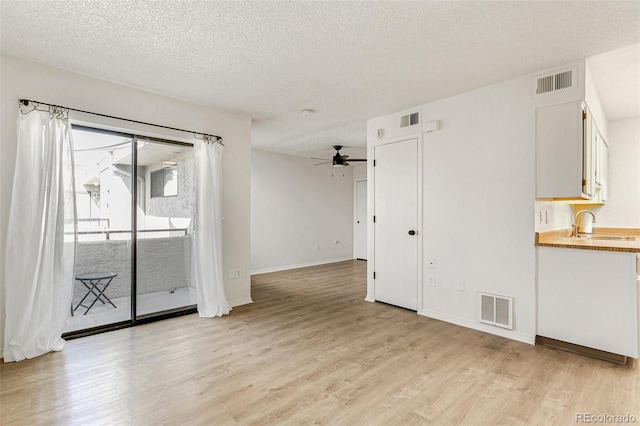 unfurnished room with visible vents, light wood-type flooring, a ceiling fan, and a sink