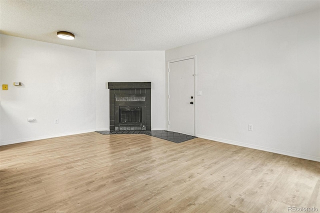 unfurnished living room with baseboards, a textured ceiling, wood finished floors, and a tile fireplace