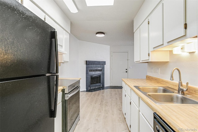 kitchen featuring light wood-style flooring, a fireplace with flush hearth, freestanding refrigerator, a sink, and electric stove