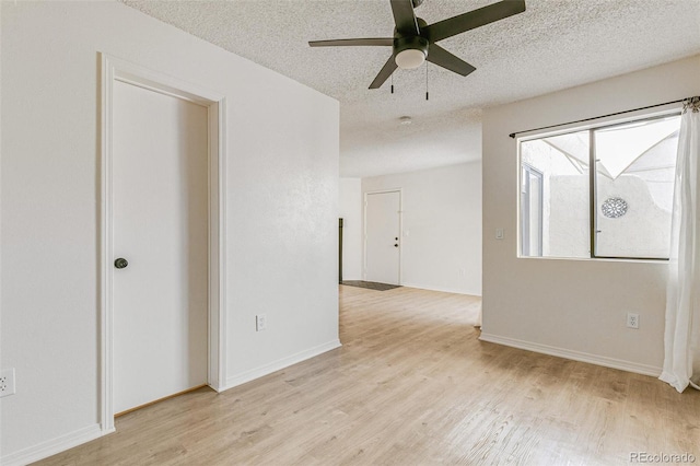 empty room featuring ceiling fan, light wood-style flooring, baseboards, and a textured ceiling