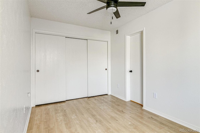 unfurnished bedroom featuring a ceiling fan, baseboards, light wood-style floors, a closet, and a textured ceiling