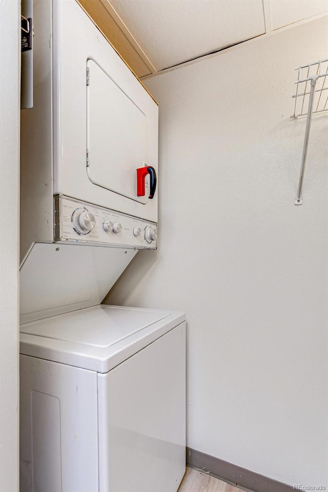 clothes washing area with baseboards, stacked washer and clothes dryer, and laundry area