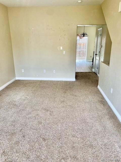 carpeted empty room with lofted ceiling and a notable chandelier