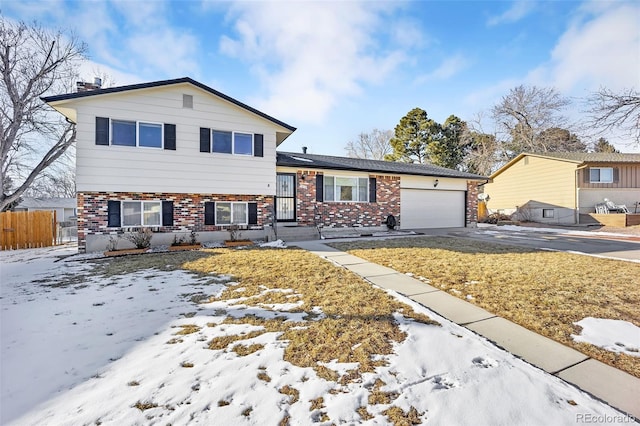 split level home featuring driveway, brick siding, an attached garage, and fence