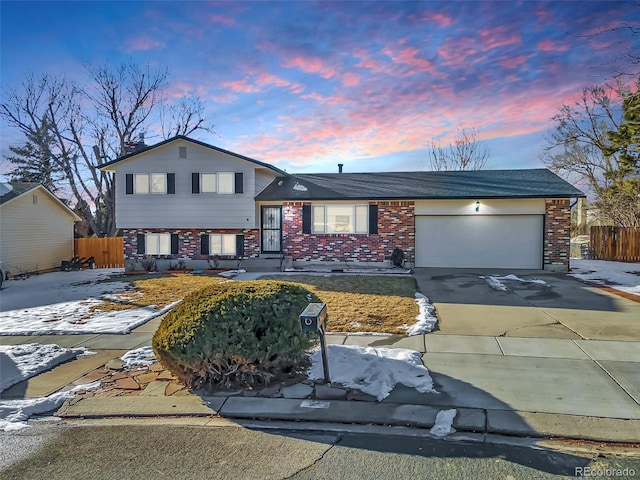 tri-level home with concrete driveway, brick siding, and fence