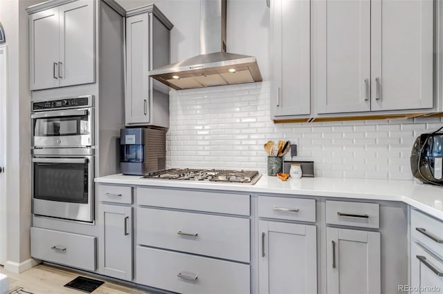 8049 Monte Vista Cir, Littleton, CO 80125 - kitchen featuring wall chimney exhaust hood, appliances with stainless steel finishes, gray cabinets, tasteful backsplash, and light countertops