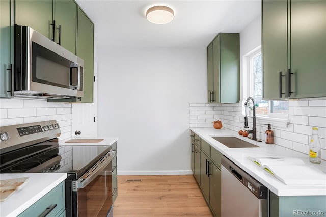 1205 W 101st Ave, Northglenn, CO 80260 - kitchen featuring appliances with stainless steel finishes, green cabinets, a sink, light wood-type flooring, and decorative backsplash