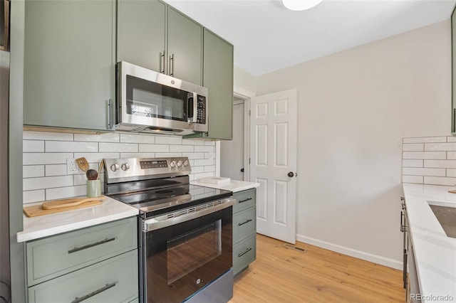 1205 W 101st Ave, Northglenn, CO 80260 - kitchen with appliances with stainless steel finishes, green cabinets, baseboards, light wood-style floors, and tasteful backsplash