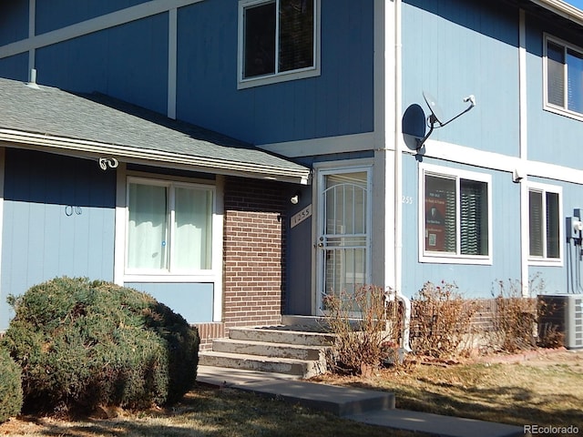 property entrance with a shingled roof and brick siding