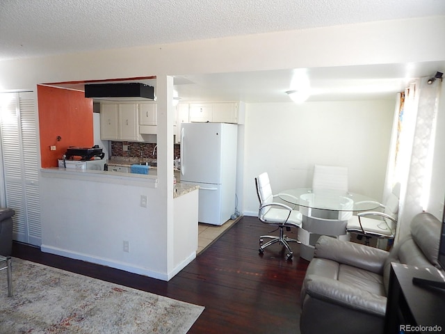 kitchen with tasteful backsplash, freestanding refrigerator, white cabinetry, a textured ceiling, and wood finished floors