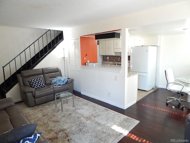 living area featuring stairs, a textured ceiling, wood finished floors, and baseboards